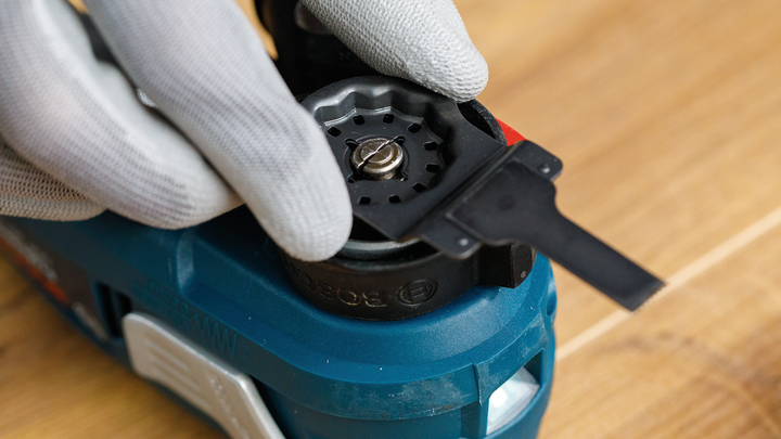 Eine Person mit Sicherheitsausrüstung installiert eine Klinge an einem blauen Elektrowerkzeug.