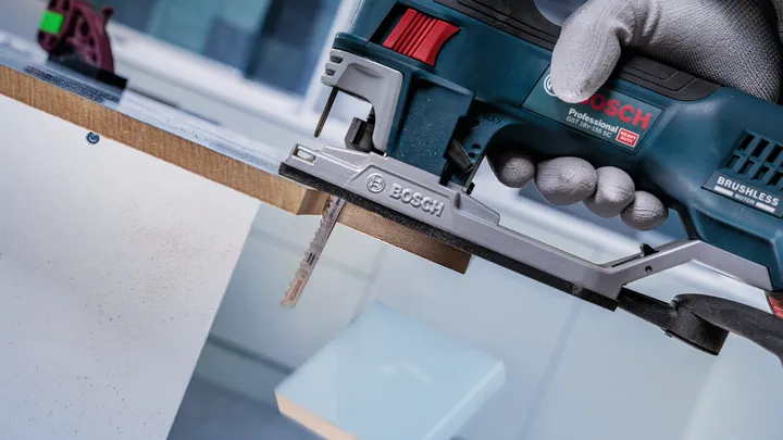 Eine Person mit Sicherheitsausrüstung schneidet mit einer Stichsäge ein Holzbrett zu.