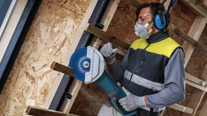 Eine Person mit Sicherheitsausrüstung schneidet Holz mit einer großen Kreissäge.