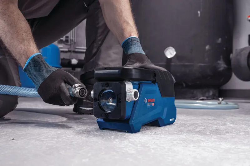 Eine Person in Schutzausrüstung schließt einen Schlauch an eine kompakte blaue Wasserpumpe an.