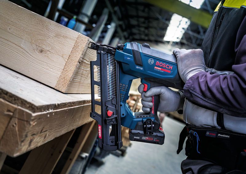 Eine Person, die Schutzausrüstung trägt, benutzt einen kabellosen Holznagler an einem Holzbalken.
