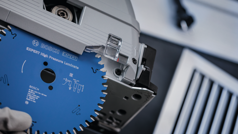 Eine Person, die Schutzausrüstung trägt, setzt ein Kreissägeblatt in ein Elektrowerkzeug ein.