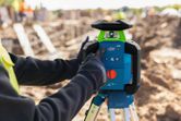 Eine Person in Schutzausrüstung justiert ein Laser-Nivelliergerät auf einer Baustelle.