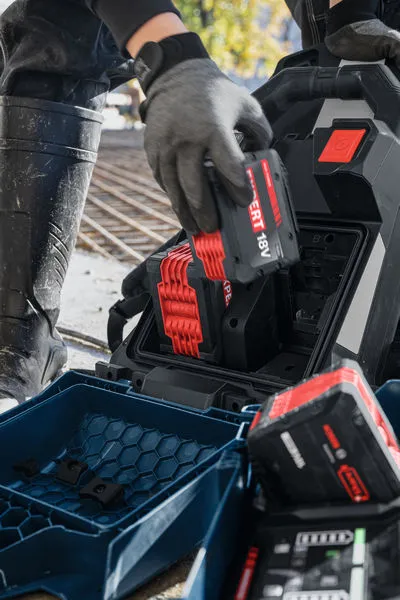 Eine Person, die Schutzausrüstung trägt, legt einen 18V-Akku vom Typ GPU18V2DI in eine Ladestation ein.