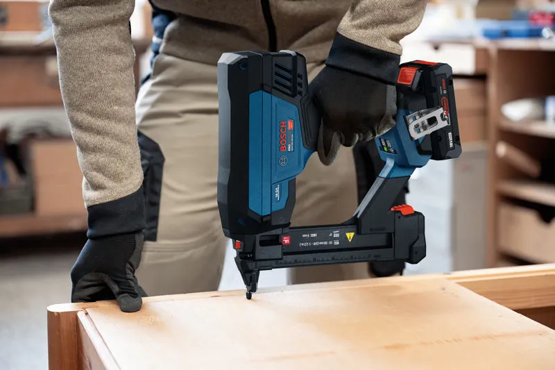 Eine Person, die Schutzausrüstung trägt, benutzt einen kabellosen Schmalrückentacker an Holz.