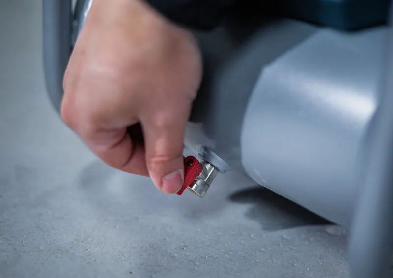 Eine Person dreht ein rotes Ventil an einer grauen zylinderförmigen Maschine.