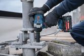 Eine Person, die Schutzausrüstung trägt, benutzt einen Akku-Schlagschrauber an einer Metallstütze.
