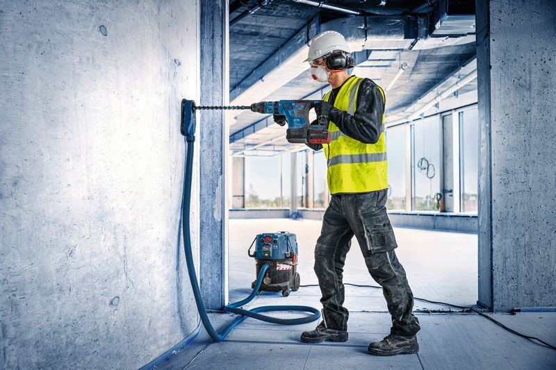Ein Arbeiter in Schutzausrüstung bohrt mit einem akkubetriebenen Bohrhammer in Beton.