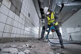 Eine Person, die Schutzausrüstung trägt, benutzt einen Bohrhammer, um Fliesenböden aufzubrechen.