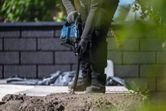 Eine Person, die Schutzausrüstung trägt, benutzt ein Elektrowerkzeug, um im Freien in Beton zu bohren.