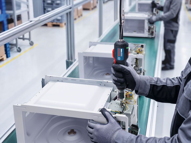 Eine Person, die Schutzausrüstung trägt, montiert mit einem Elektrowerkzeug elektronische Geräte an einer Produktionslinie.