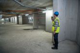 Eine Person, die Schutzausrüstung trägt, benutzt ein Laser-Nivelliergerät in einem Betongebäude.