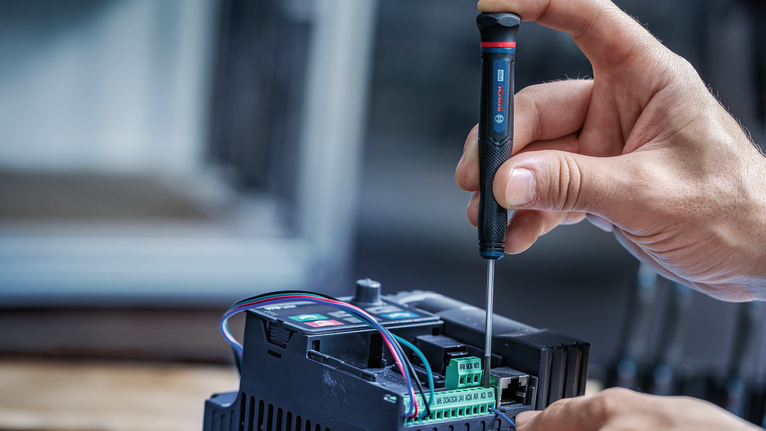 Eine Person benutzt einen Schraubendreher, um die Verkabelung eines elektronischen Geräts anzupassen.