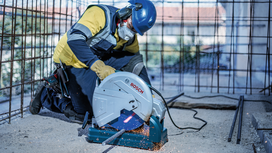 Eine Person, die Schutzausrüstung trägt, schneidet Bewehrungsstahl mit einer Metallsäge, wodurch Funken entstehen.