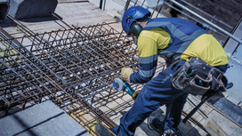 Eine Person, die Schutzausrüstung trägt, benutzt ein Elektrowerkzeug, um auf einer Baustelle Bewehrungsstahl zu durchtrennen.