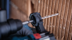 Eine Person in Schutzausrüstung bohrt in eine strukturierte braune Wand.