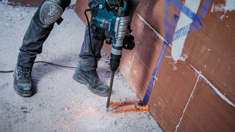Eine Person in Schutzausrüstung bohrt auf einer Baustelle in Beton.