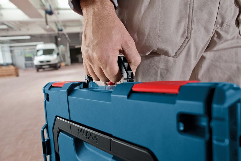 Person, die einen blauen Werkzeugkoffer in einem Werkstattbereich trägt.