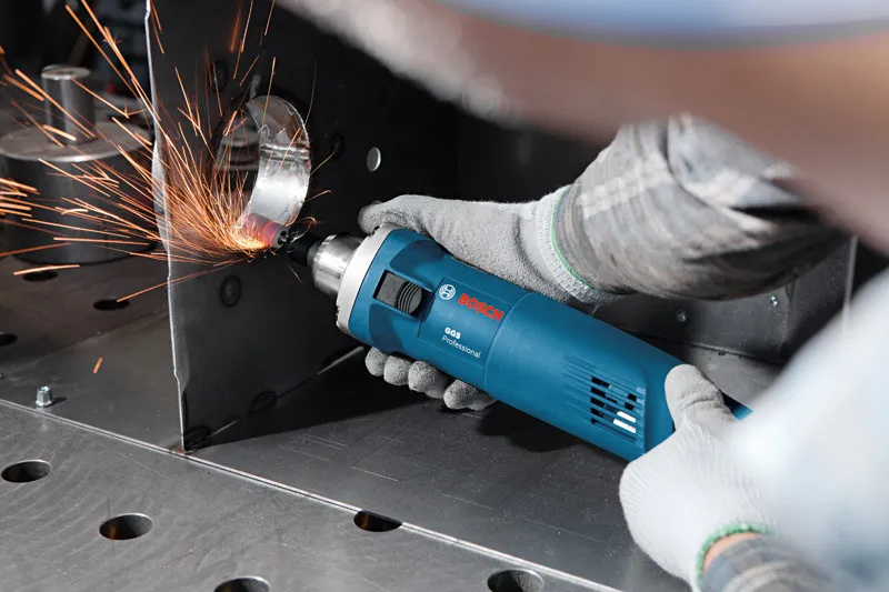 Eine Person mit Schutzausrüstung schleift mit einem Elektrowerkzeug eine Metallkante, wodurch Funken entstehen.