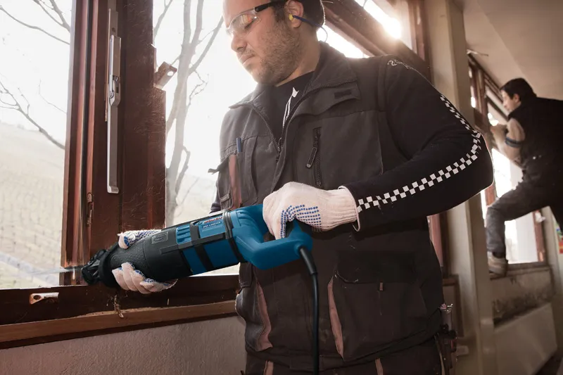 Eine Person mit Sicherheitsausrüstung schneidet mit einer Säbelsäge einen Fensterrahmen durch.