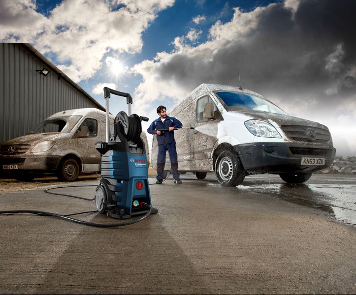 Une personne portant un équipement de sécurité utilise un nettoyeur haute pression pour nettoyer une camionnette sale à l'extérieur.