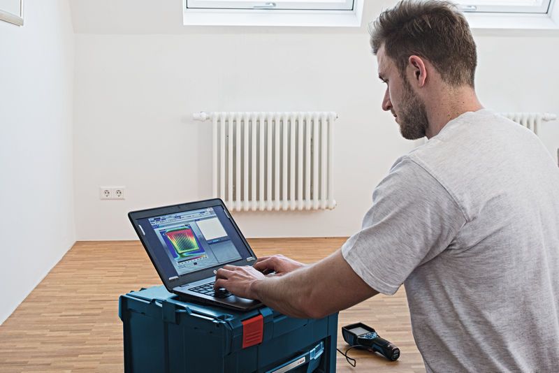 Une personne analysant les données d'une caméra thermique sur un ordinateur portable dans une pièce équipée d'un radiateur.