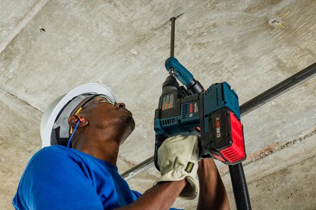 Une personne portant un équipement de sécurité perce un plafond en béton.