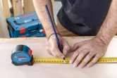 Personne marquant une mesure sur du bois avec un crayon à l'aide d'un ruban à mesurer.