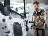 Une personne portant un équipement de sécurité utilise un outil électrique pour fixer des pièces sur une porte de véhicule.