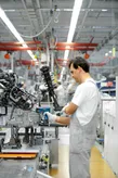 Une personne portant un équipement de sécurité utilise un outil électrique pour assembler des machines sur une chaîne de production.