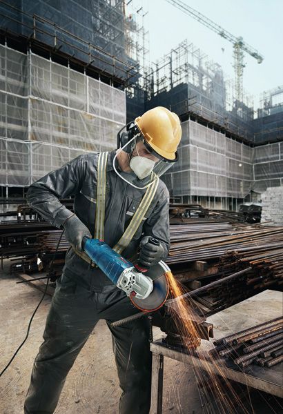 Une personne portant un équipement de sécurité meule des barres métalliques avec une meuleuse d'angle sur un chantier de construction.