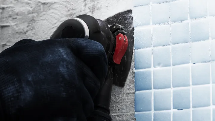 Une personne portant un équipement de sécurité coupe des carreaux blancs avec un outil électrique.