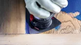 Une personne portant un équipement de sécurité utilise un outil multifonction pour poncer la peinture sur du bois.