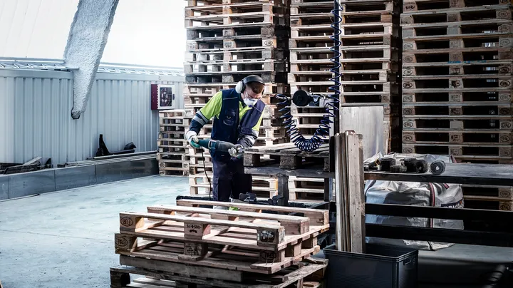 Une personne portant un équipement de sécurité utilise un outil électrique pour couper des palettes en bois.