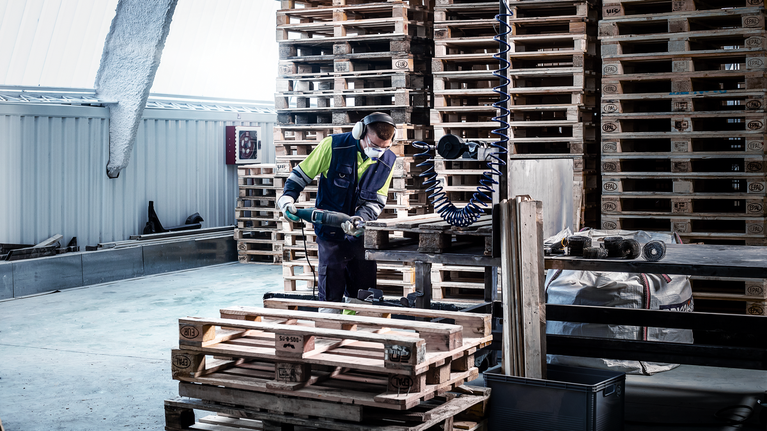 Une personne portant un équipement de sécurité utilise un outil électrique pour couper des palettes en bois.