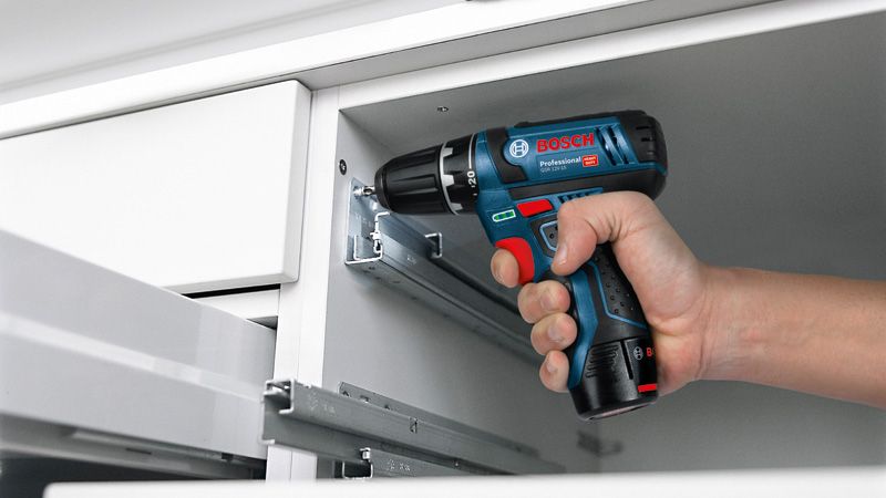 Une personne utilise une perceuse-visseuse sans fil pour fixer une vis dans le cadre d’une armoire.
