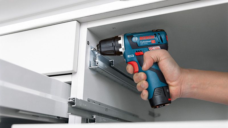 Une personne utilise une perceuse sans fil pour assembler un tiroir à l’intérieur d’une armoire.