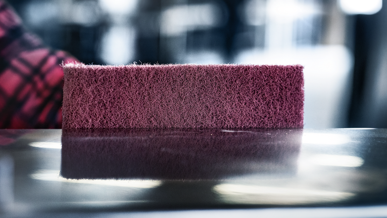 Un tampon abrasif marron repose sur une surface métallique brillante.