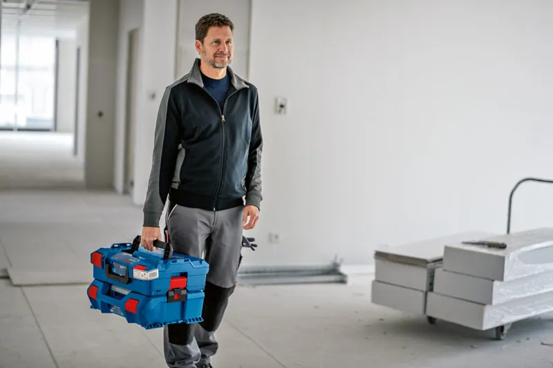Personne portant un système de mallette de transport empilable bleu avec loquet dans une zone de construction.