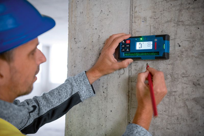 Une personne portant un équipement de sécurité utilise un récepteur laser pour marquer des mesures sur un mur en béton.