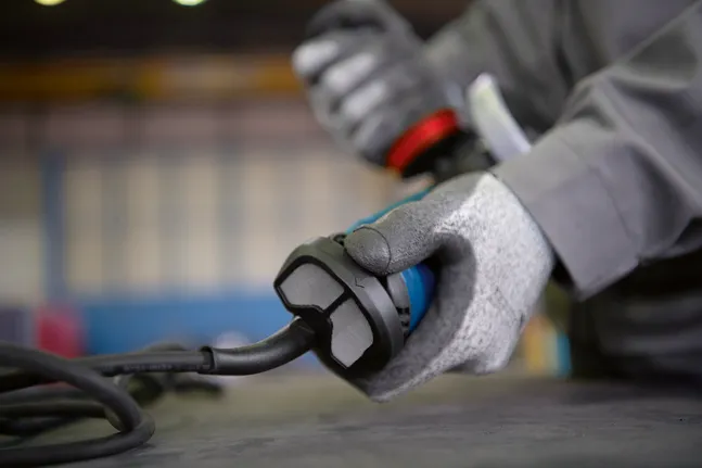 Une personne portant un équipement de sécurité tient un outil électrique filaire sur un établi.