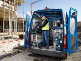Une personne portant un équipement de sécurité organise des outils électriques dans une camionnette sur un chantier de construction.
