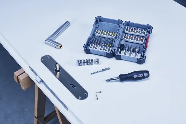 Un jeu de tournevis et des embouts assortis disposés sur une table avec des composants de serrure de porte.