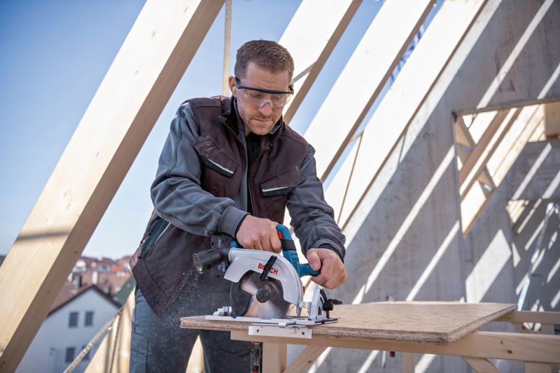 Une personne portant un équipement de sécurité utilise une scie circulaire pour couper du contreplaqué sur un chantier de construction.