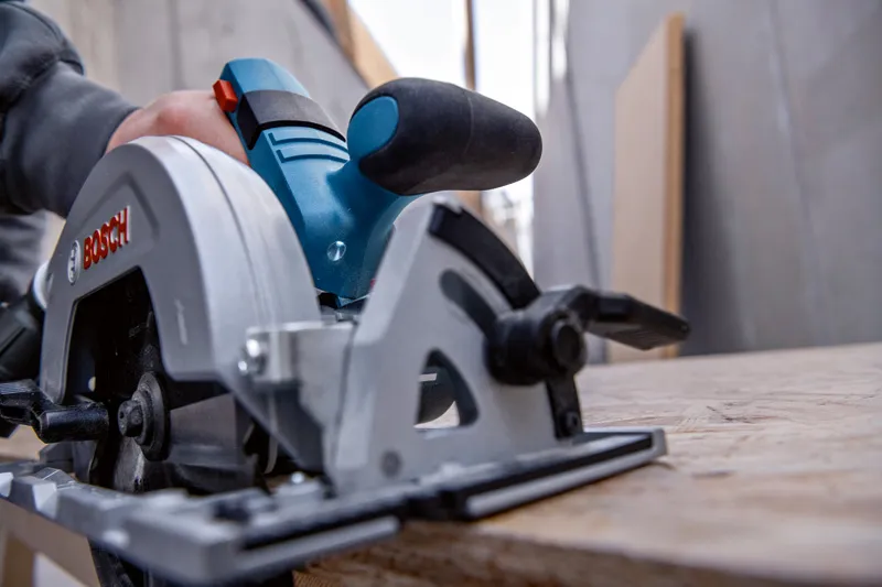 Une personne guide une scie circulaire le long d'une planche de bois dans un atelier.