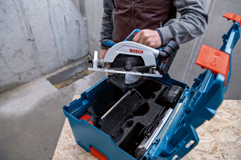 Une personne place une scie circulaire dans une boîte à outils bleue sur une surface en bois.