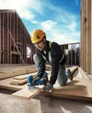 Une personne portant un équipement de sécurité coupe du contreplaqué avec une scie sauteuse sur un chantier de construction.