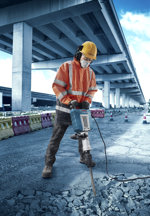 Une personne portant un équipement de sécurité utilise un marteau de démolition pour briser le béton sur un chantier routier.