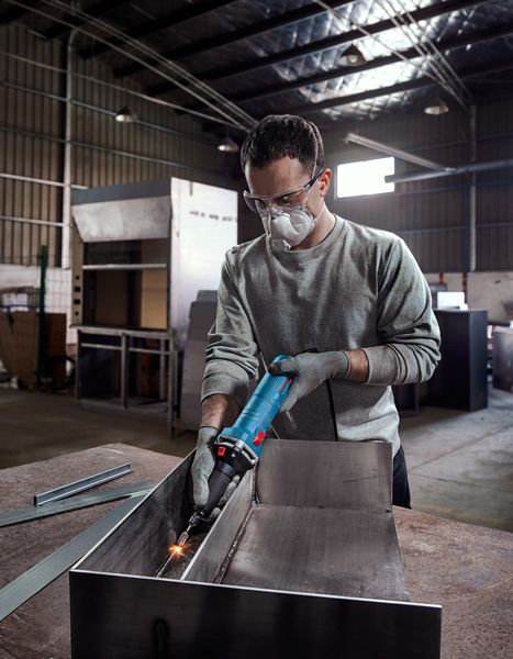 Une personne portant un équipement de sécurité broie du métal dans un atelier industriel.