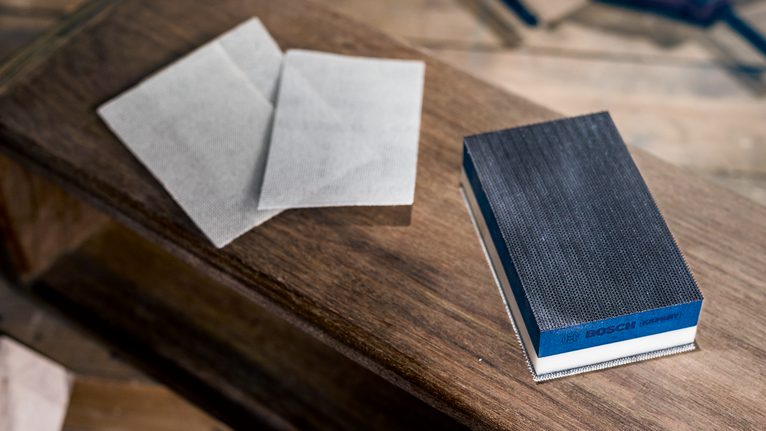 Bloc de ponçage manuel et feuilles abrasives sur une surface en bois.